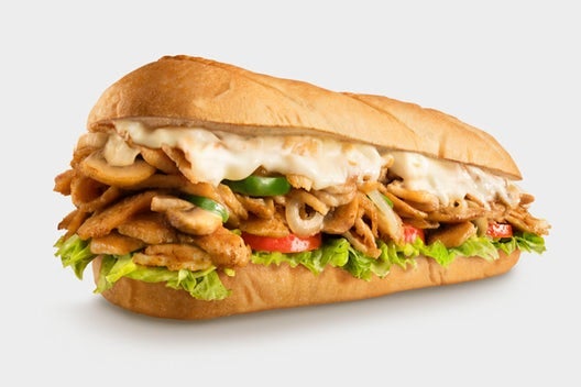 Chicken Cheese steak or chicken phillies from Charleys cheesesteak restaurants served on a toasted roll with grilled chicken, provolone, peppers, onions, lettuce, tomato, mayo, and pickle, displayed against a white background